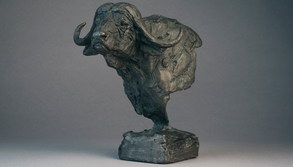 Bronze buffalo sculpture with textured surface on a square base against a gray background.