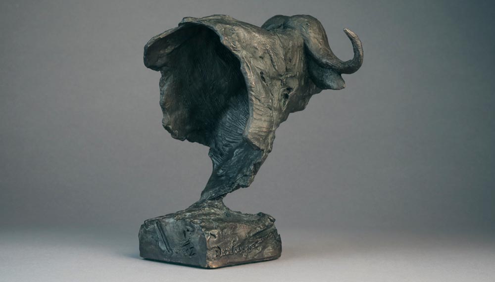 Bronze sculpture of a buffalo head with a curved horn on a rectangular base.