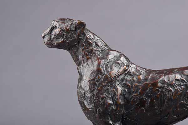 Close-up of a textured bronze cheetah sculpture on a gray background.