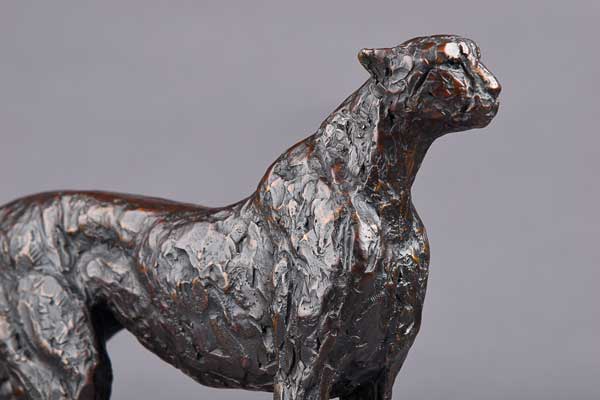 Close-up of a textured bronze sculpture of a cheetah against a gray background.