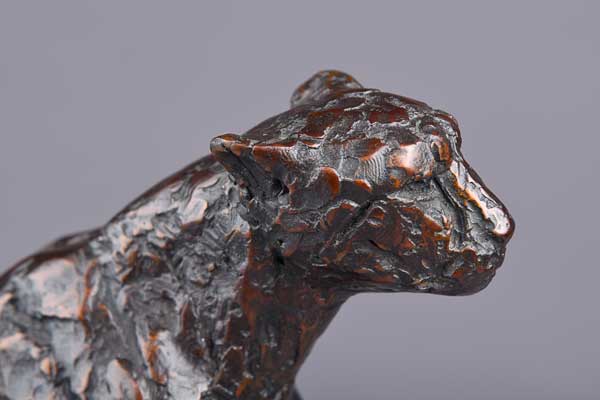 Close-up of textured bronze cheetah sculpture's head and upper neck on gray background.