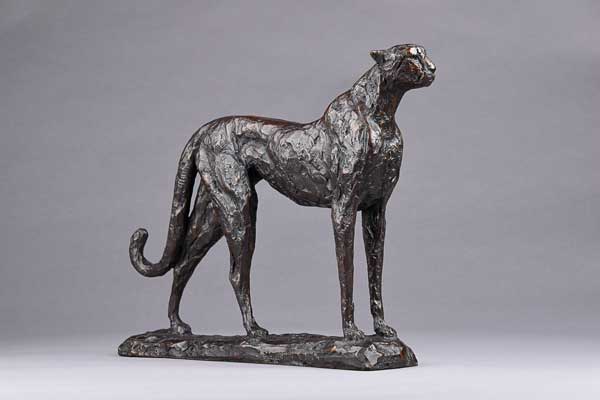 Bronze sculpture of a standing cheetah on a rectangular base against a gray background.