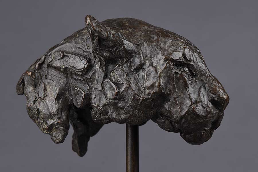 Metal sculpture of a large cat's head with detailed facial features on a stand.