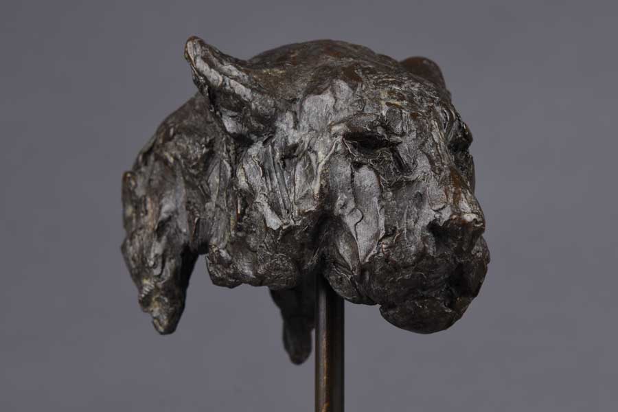 Bronze sculpture of a leopard's head mounted on a stand against a gray background.