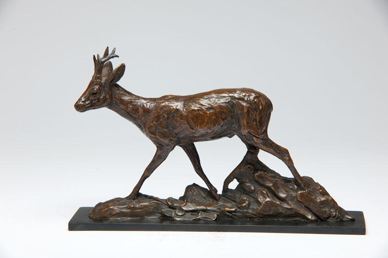 Bronze sculpture of a roe buck walking on textured base resembling rocks and leaves.