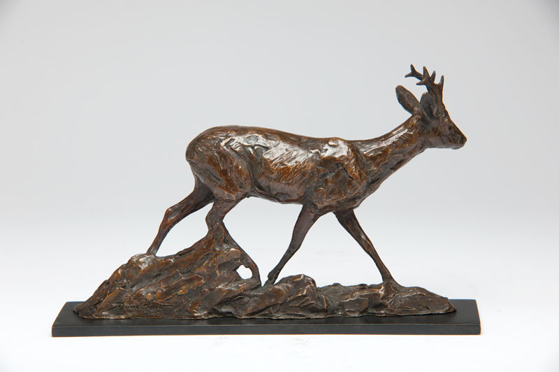 Bronze sculpture of a roe buck walking on a rocky base with detailed texture.