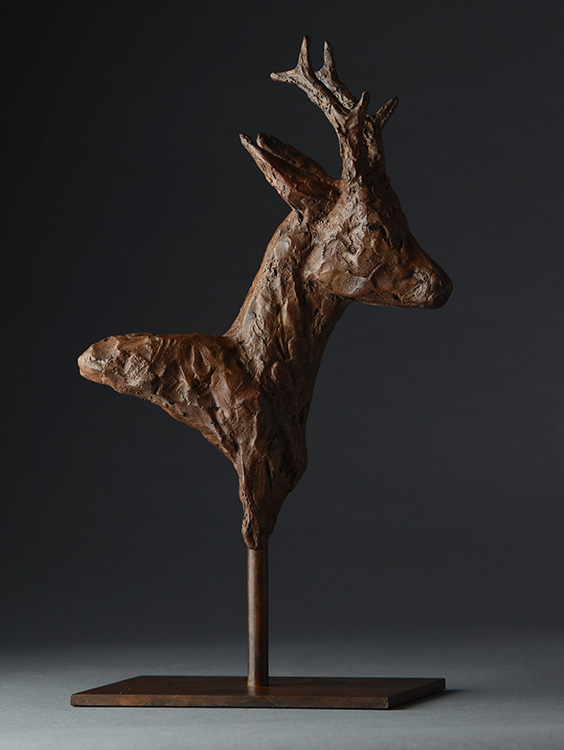 Bronze sculpture of a roe deer head and neck mounted on a stand against a dark background.