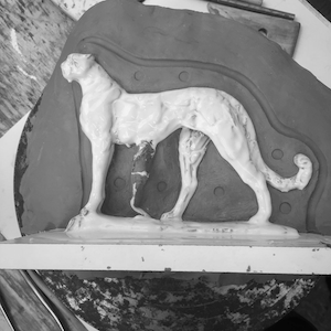 White sculpture of a standing dog with a wrapped front leg on a display platform.